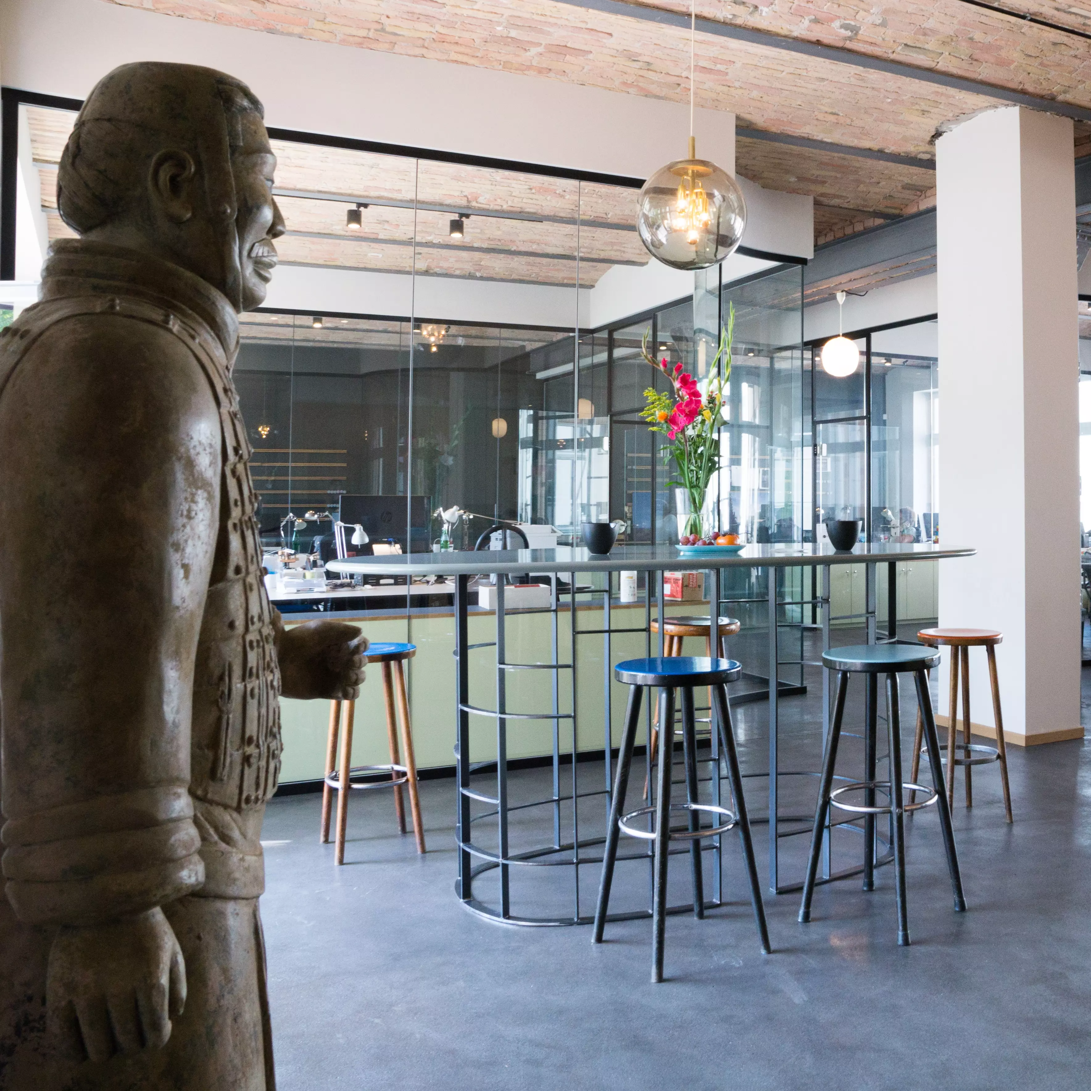 A dining bar area with stools in front of glass-walled workspaces.