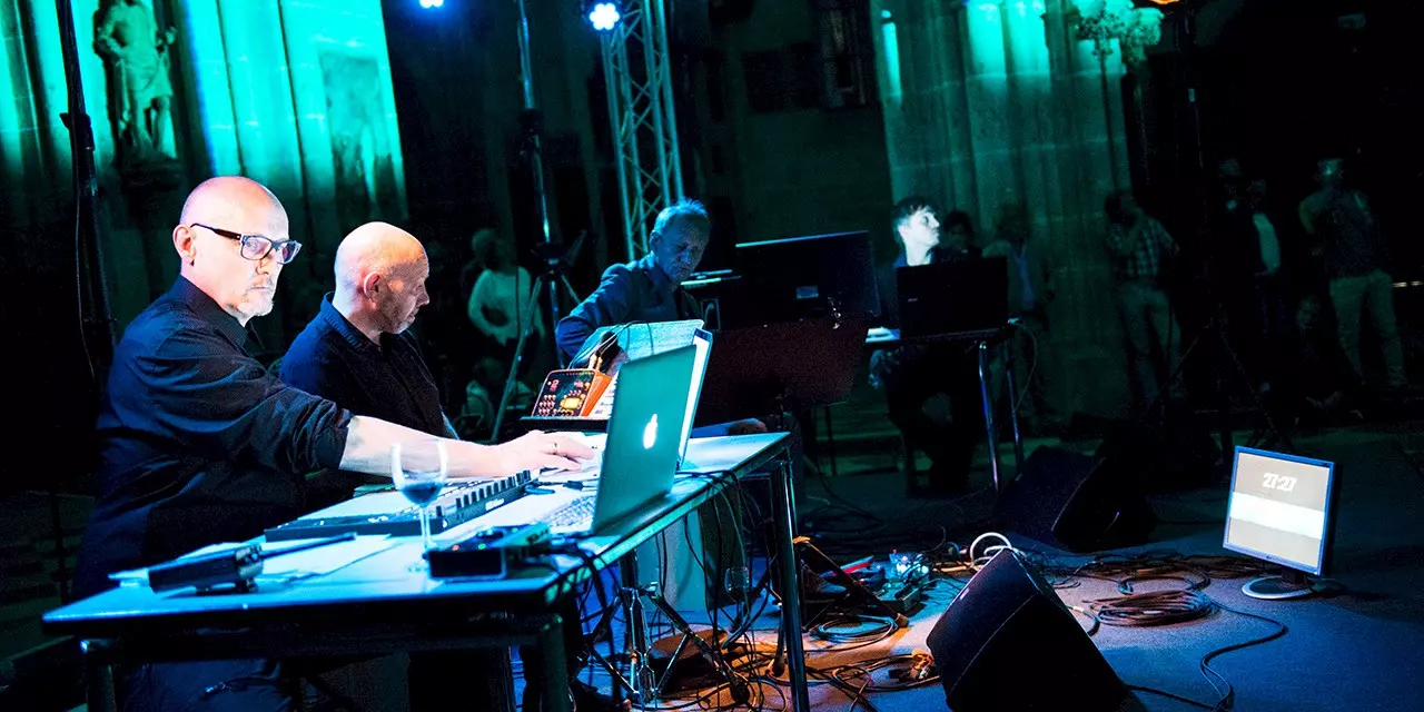 Musicians with laptops and electronic equipment performing live at Ulm Minster, atmospherically lit in shades of blue and green.